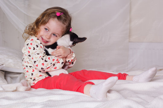 Baby girl sitting on bed and holding dog