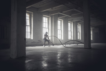 Black woman tossing ropes in dark gym