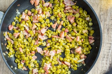 Green peas, bacon and onion fried in frying pan, home cooking