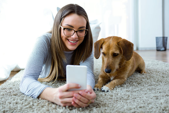 Beautiful young woman with her dog using mobile phone at home. - Powered by Adobe