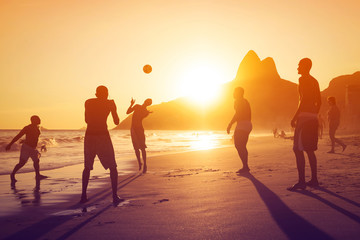 Silhouette of locals playing ball at sunset in Ipanema Beach, Rio de Janeiro, Brazil.