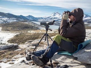 Man in the mountains looking through binoculars under blue sky