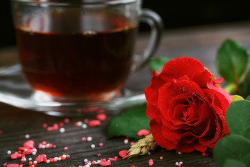 Tea in a transparent cup, color candies and a red rose