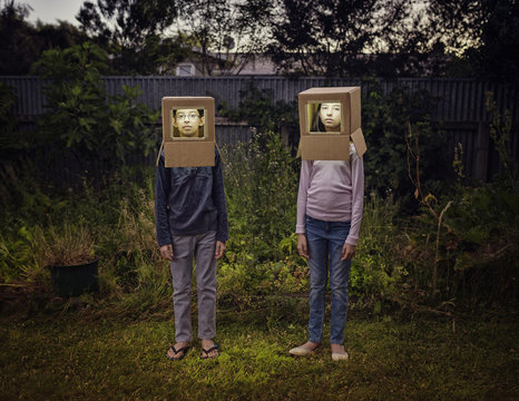 Mixed race children wearing cardboard astronaut helmets in backyard