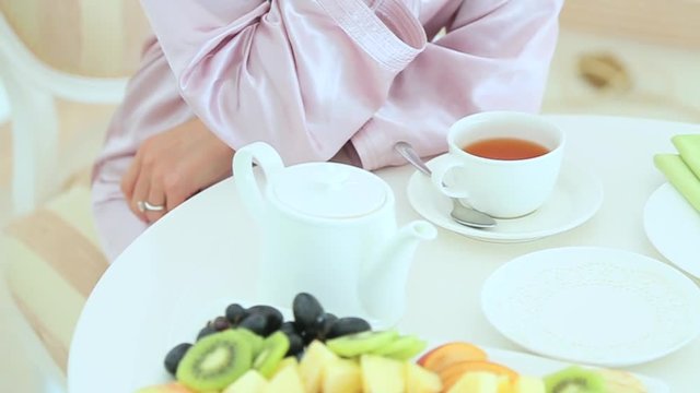 Woman in bathrobe drinking tea at beautifully laid table.
