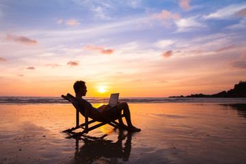 silhouette of happy business man with laptop working on the beach.