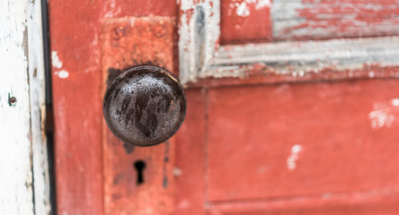 Simple, old 1920's era Door knob with skeleton keyhole on an old, paint chipped, red door.  Detail of ice water on an old, well worn, metal doorknob outside.