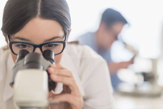 Young female scientist looking through microscope 