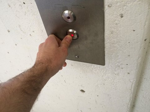 Hand pressing down button on elevator call panel
