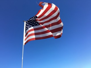 Obraz premium A torn American flag flying against a blue sky. 