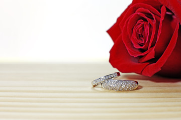 Two wedding rings on the wooden table with dark red rose background, love concept for valentines day