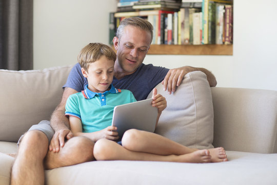 Caucasian father and son using digital tablet on sofa
