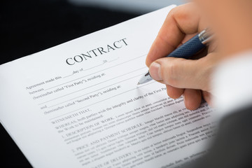 Close-up Of Businessman Hand Holding Pen Over Contract Form