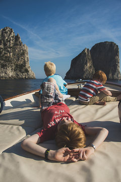 Caucasian brothers on boat admiring rock formations and ocean, Isle of Capri, Naples, Italy