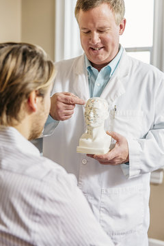 Caucasian acupuncturist showing patient carved bust with diagram