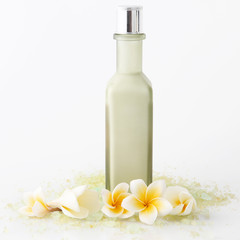 Obraz na płótnie Canvas Green cosmetic bottle with bath salt and frangipani flowers