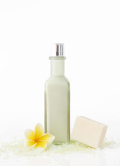 Obraz na płótnie Canvas Green cosmetic bottle with soap bar and frangipani flowers