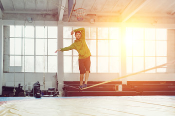 Man slacklining walking and balancing on a rope, slackline in a sports hall