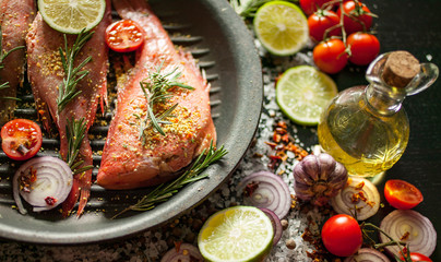 Fototapeta na wymiar Fillet of sea fish on a grill with vegetables and spices against a dark background