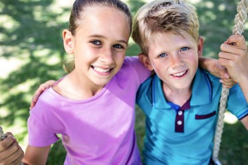 Siblings sitting on a swing in the park