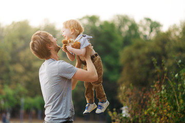 Young and happy father plays with his young son in the summer park