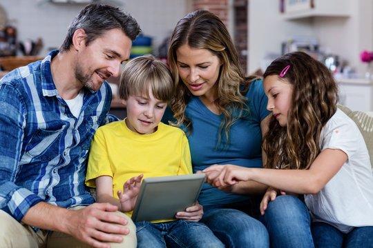 Parents And Kids Sitting On Sofa And Using A Digital Tablet