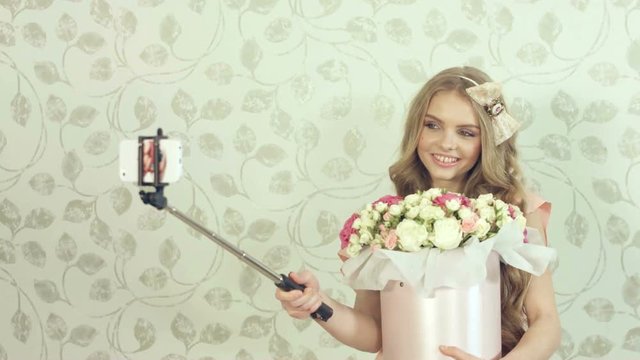 Cute girl with a large bouquet of roses doing selfie using a monopod in the studio 