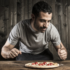 Ragazzo con i capelli scuri con la pizza in mano su sfondo legno scuro poggiato su un tavolo di legno