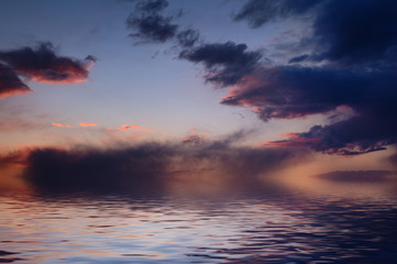 Dramatic sunset with sun and clouds reflected in water.