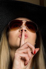 Close-up of attractive brunette woman in a bikini, big hat and sunglasses putting a finger on her...