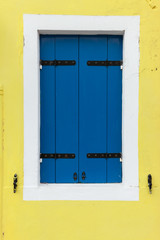 Old window with blue shutters on light yellow wall