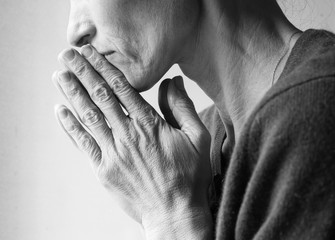 Mature woman in profile with hands clasped in prayer (cropped and black and white)
