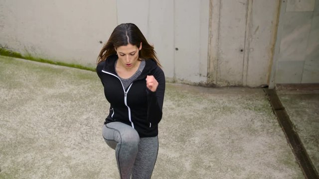 Sporty woman doing step up exercise on urban stairs for hiit workout outside. Female athlete doing knee raises cardio training..
