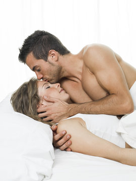 man kissing his partner sweetly in white bed