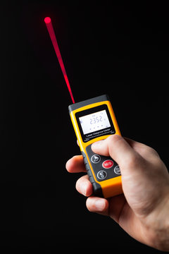 laser distance meter in hand, black background