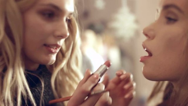 Makeup artist applies lipstick on lips of model