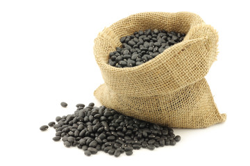 dried black beans in a burlap bag on a white background