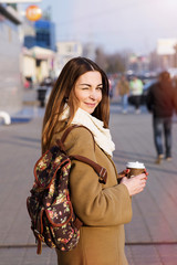 Beautiful brunette woman holding a bag and cup of hot tea or coffee, standing in the street