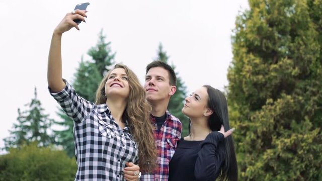 Smiling boy and girls taking a selfie on the green trees background. Slowly