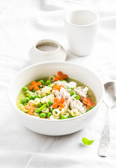 Chicken soup with vegetables and pasta on a light background