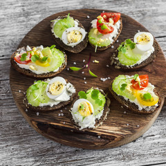 Sandwiches with soft cheese, quail eggs, cherry tomatoes and celery. Delicious healthy snack or Breakfast. On a wooden rustic board