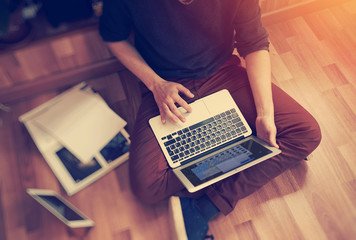 Photo of man sitting in studio on the floor, holding modern laptop hands and working with notebook. Blurred background. Horiontal