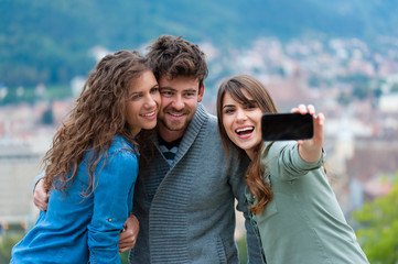 Friends taking selfportrait with mobile phone, outdoors.