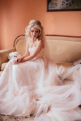 Fototapeta na wymiar Gorgeous blonde bride in stylish wedding dress posing on sofa