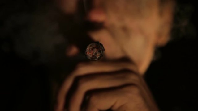 Man in a dark room, smoking a cigar.