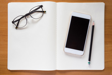 Cell phone, eyeglasses, and pencil on white notebook