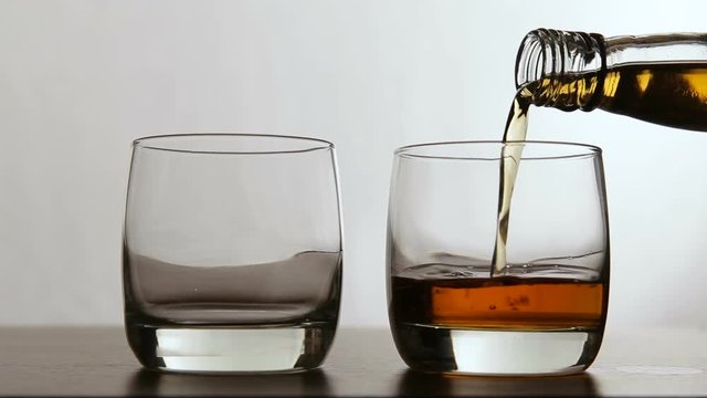 Pouring whiskey into glasses.Poured from a bottle of whiskey in the glasses on a white background.