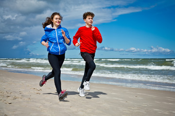Teenage girl and boy running, jumping on beach
