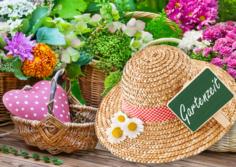 Gartenzeit - Gartenutensilien mit Blumen, Gartentisch und Strohhut