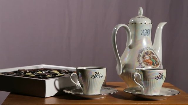 Chocolate candies and tea set on a wooden table.Cup of hot blak tea with chocolate candy.Porcelain tea set on an black background.Two teacups and teapot.Vintage tea set for two persons.